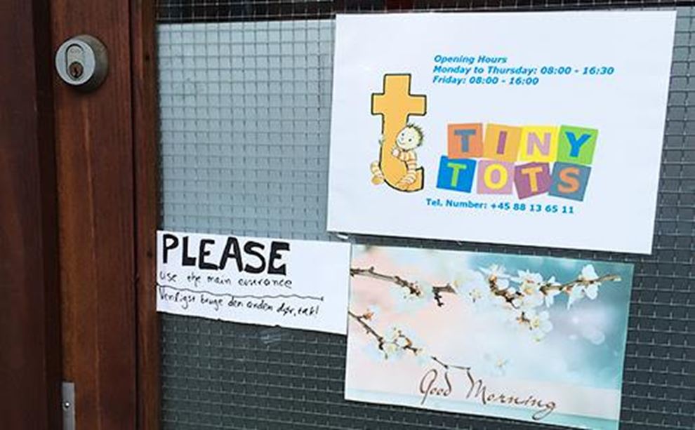 Yderdør hvor der hænger sedler, blandt andet et opslag med Tiny Tots' åbningstider 